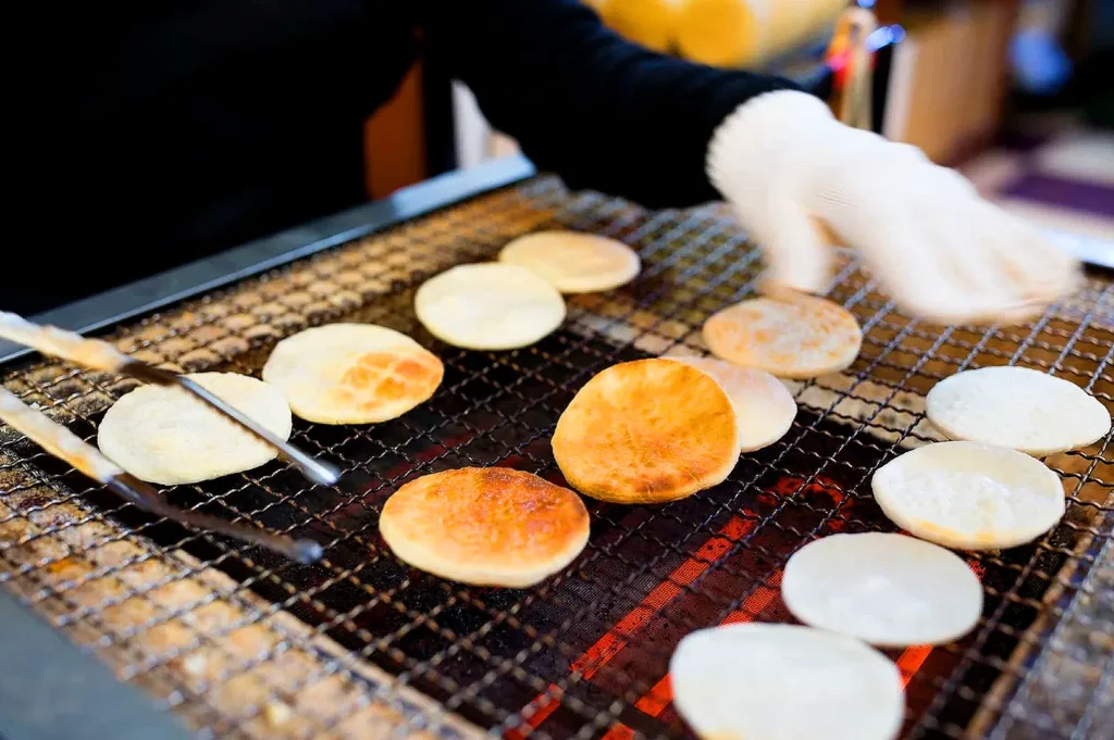 Handmade Kyoto senbei rice crackers grilling over charcoal as an artisan turns freshly toasted Japanese rice crackers for an authentic soy-glazed finish.