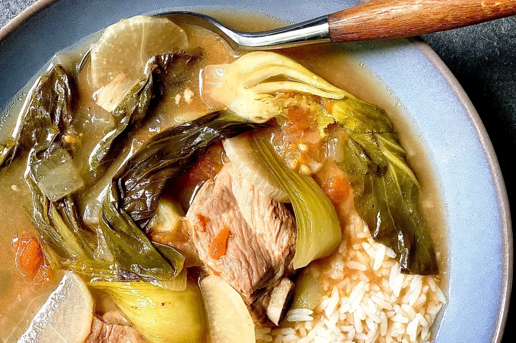 Hearty Filipino pork sinigang served with steamed rice, featuring tamarind broth, bok choy, radish, tomatoes, and vegetables.
