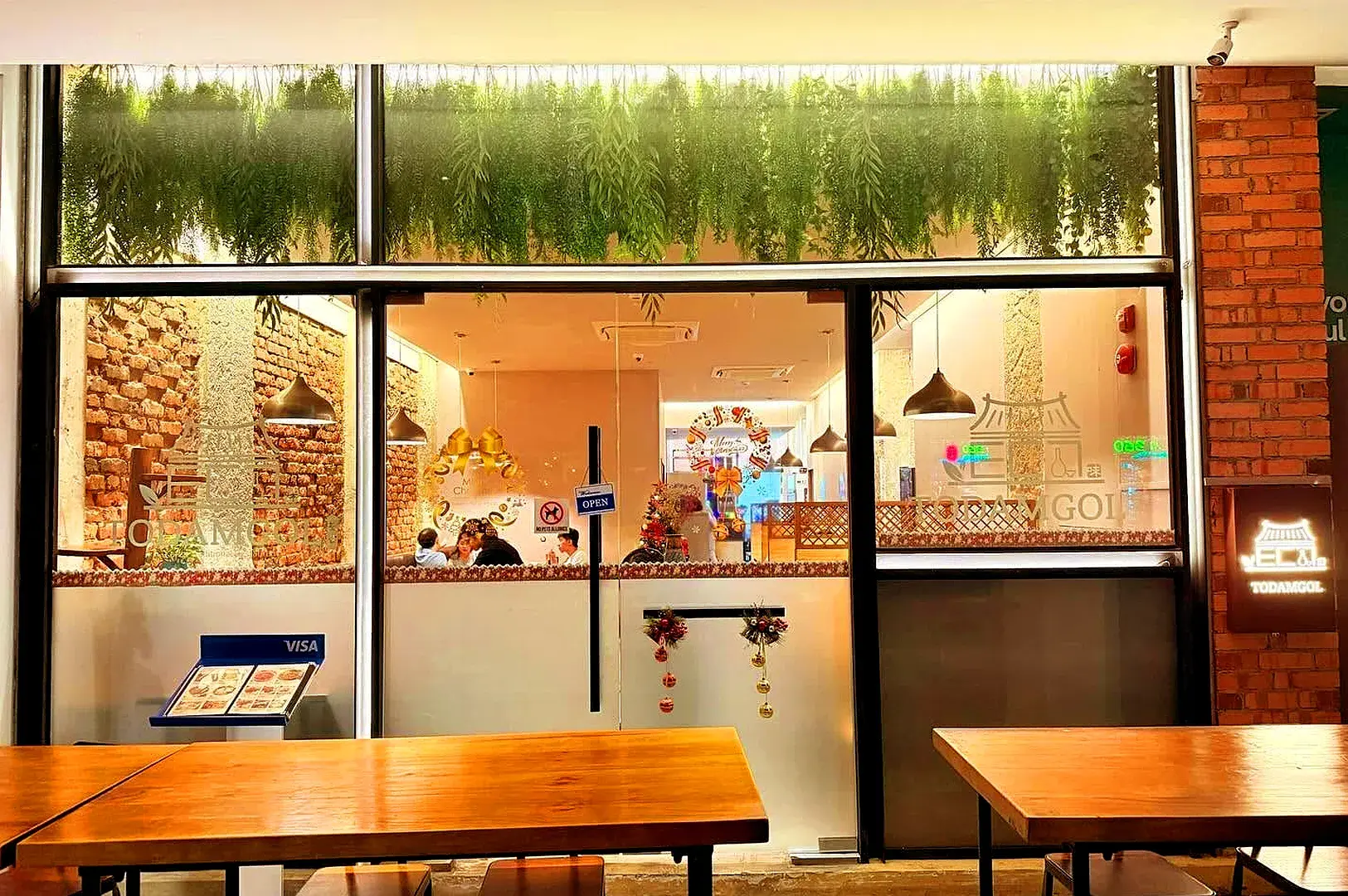 Todamgol Korean restaurant entrance and dining area with warm lighting, brick wall decor and wooden tables in Singapore