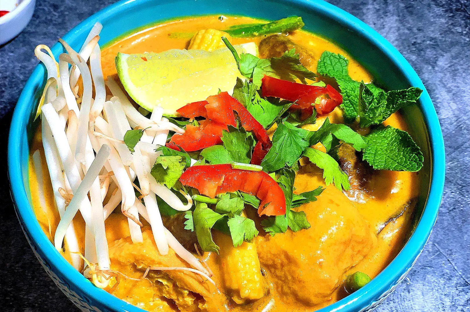 Singapore-style vegetarian laksa with creamy coconut curry broth, tofu puffs, bean sprouts, fresh herbs, lime wedge, and plant-based ingredients