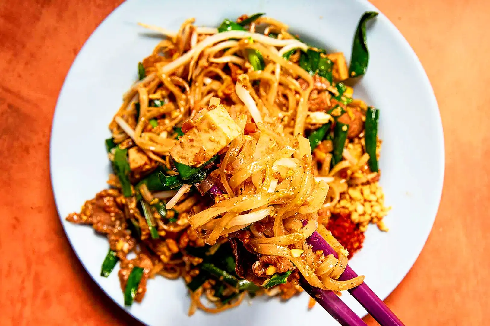 Homemade Pad Thai noodles with bean sprouts, tofu, chives, crushed peanuts and Thai chili served on a white plate