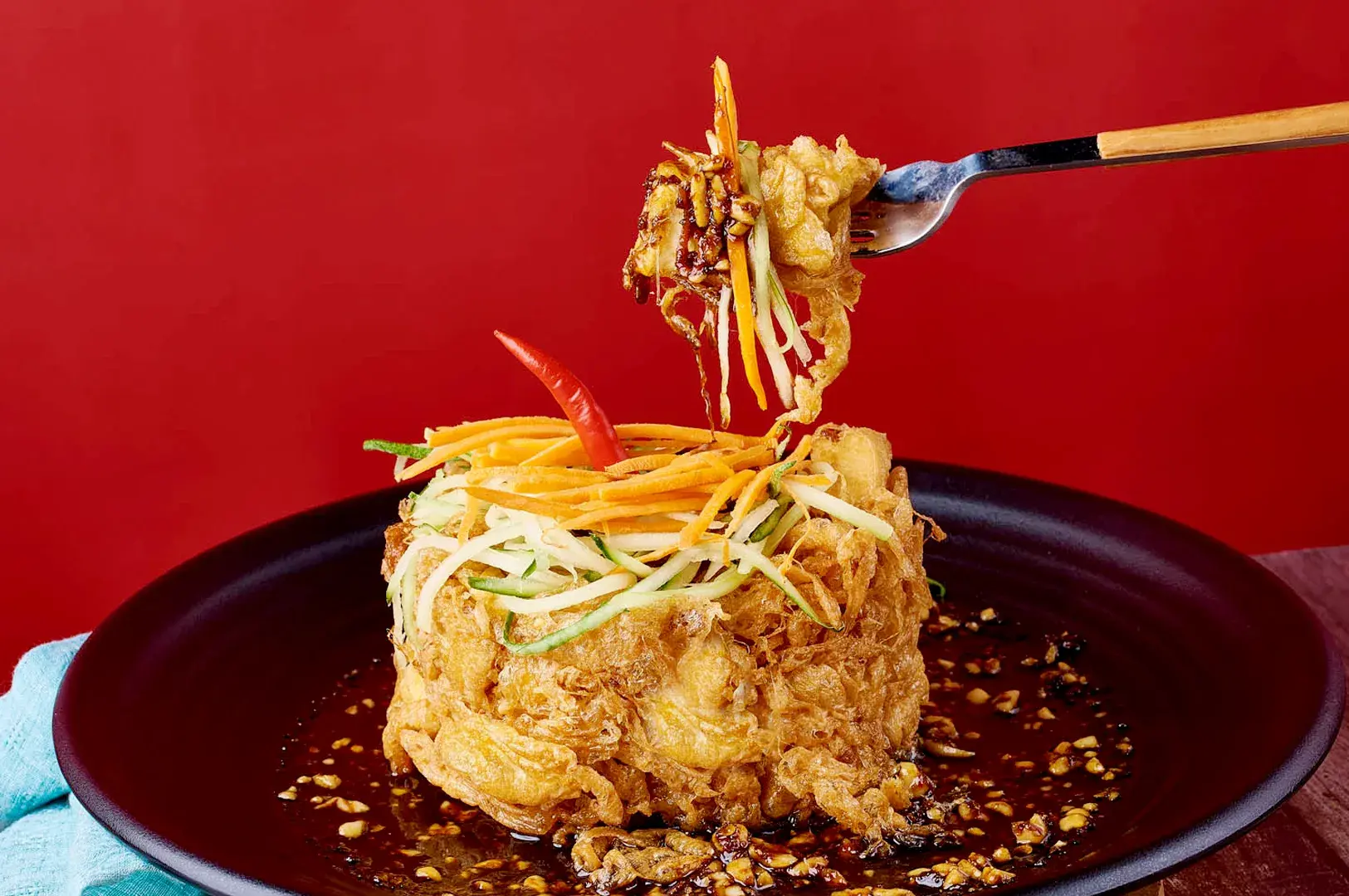Crispy Indonesian-style tofu dish with shredded vegetables, cucumber, carrots, chili, and sweet soy sauce served on a black plate at Bebek Goreng Pak Ndut.