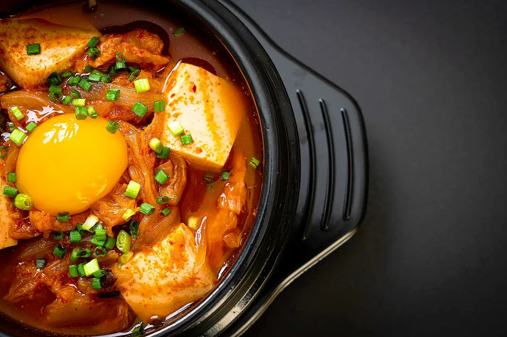 Korean kimchi stew with tofu, egg and green onions served in a traditional black stone bowl