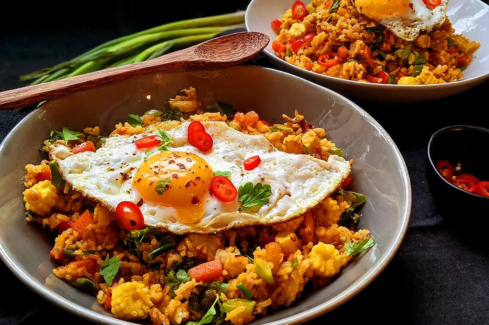 Chicken nasi goreng with fried egg, red chilies, vegetables, and herbs served in a bowl