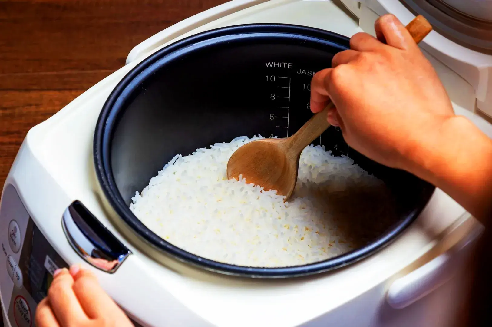 Freshly cooked white rice in a rice cooker being served with a wooden spoon