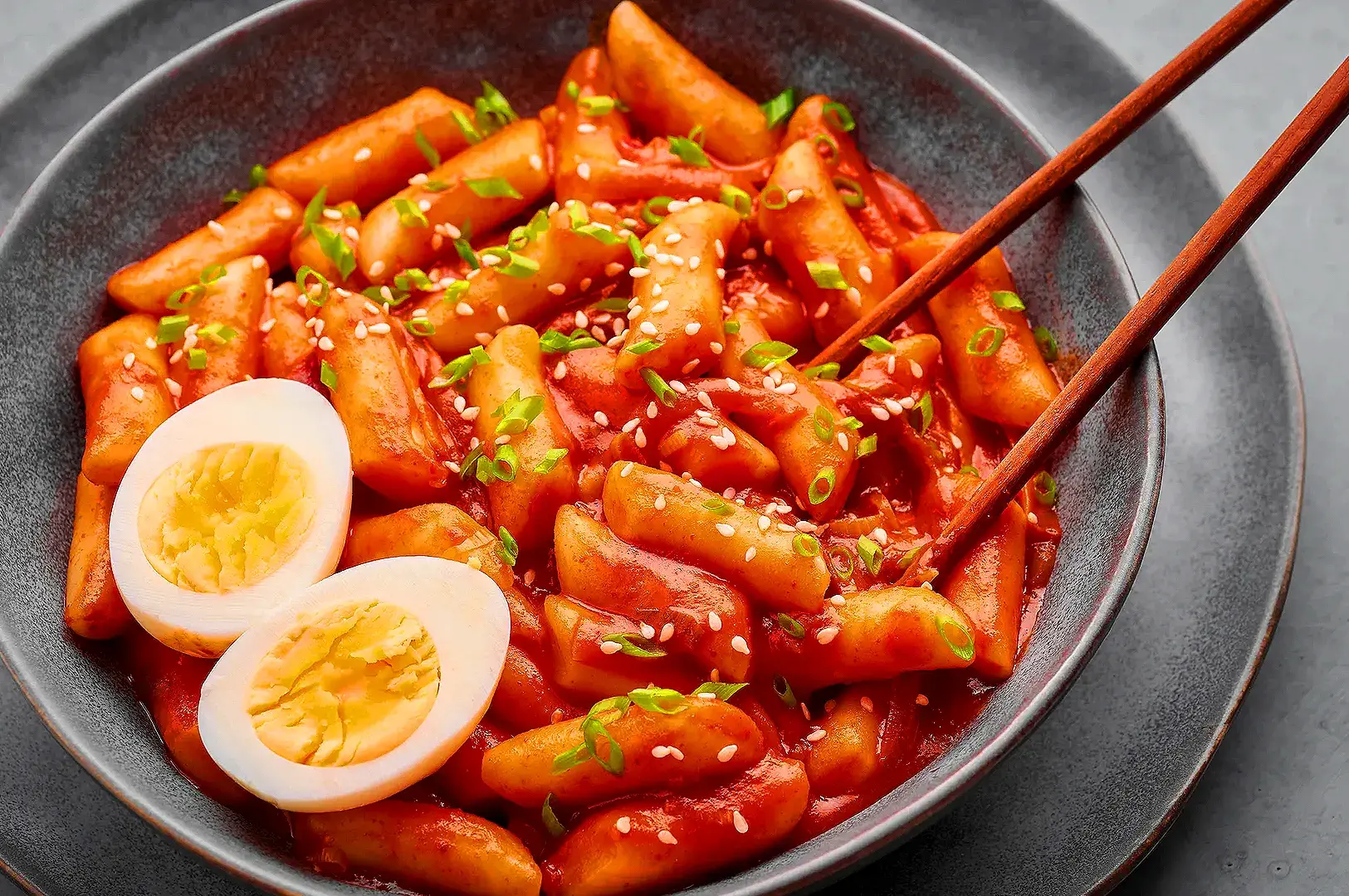 Korean tteokbokki rice cakes in spicy red sauce topped with sesame seeds and green onions