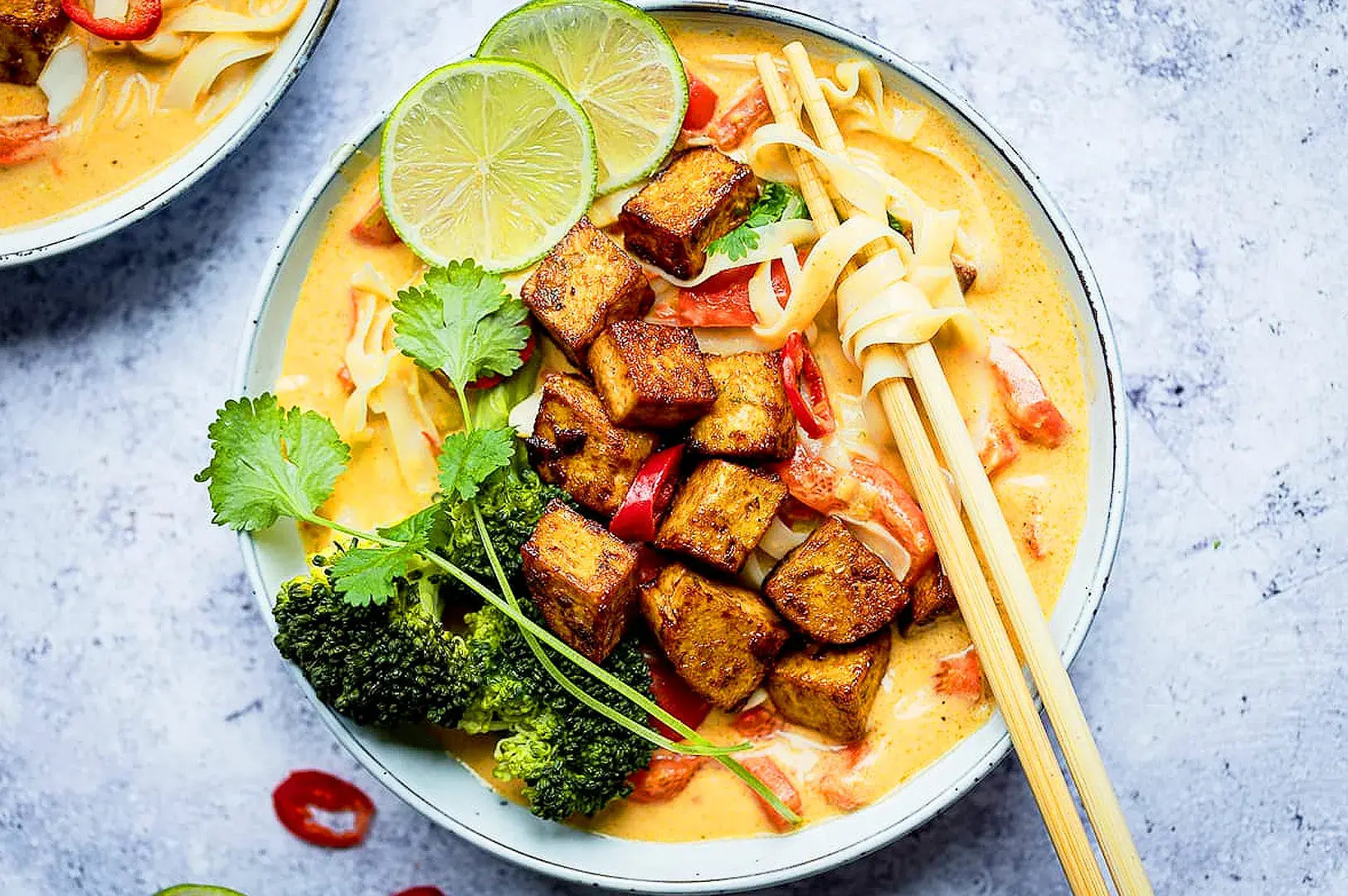 Homemade vegetarian laksa recipe featuring coconut curry broth, rice noodles, crispy tofu, broccoli, fresh lime, and Asian herbs