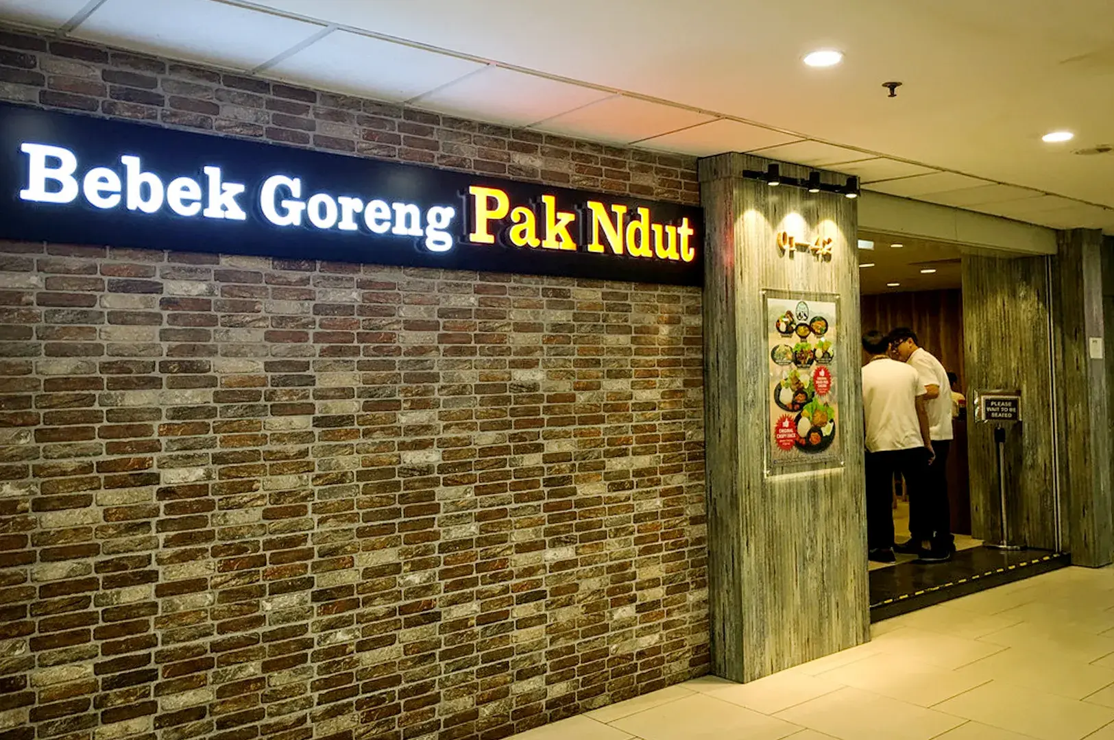 Bebek Goreng Pak Ndut restaurant entrance with illuminated sign and brick wall design
