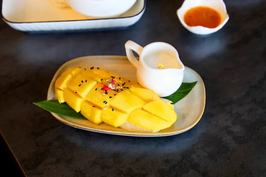 Chiang Mai mango sticky rice with fresh ripe mango slices, coconut sauce and sesame seeds on a banana leaf