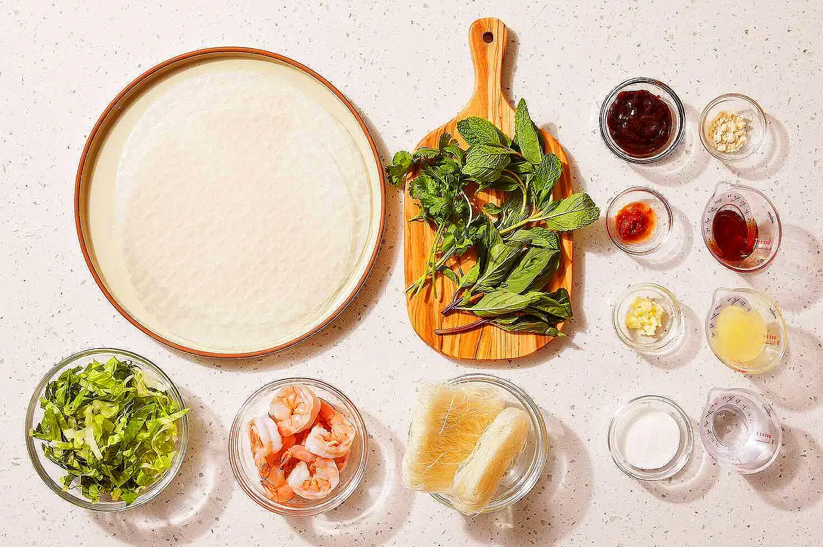 Vietnamese spring roll ingredients with rice paper, fresh herbs, shrimp, vegetables and dipping sauces