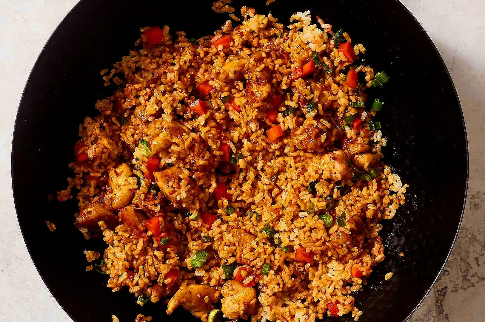 Spicy sambal fried rice with diced chicken, carrots and spring onion served in a black bowl