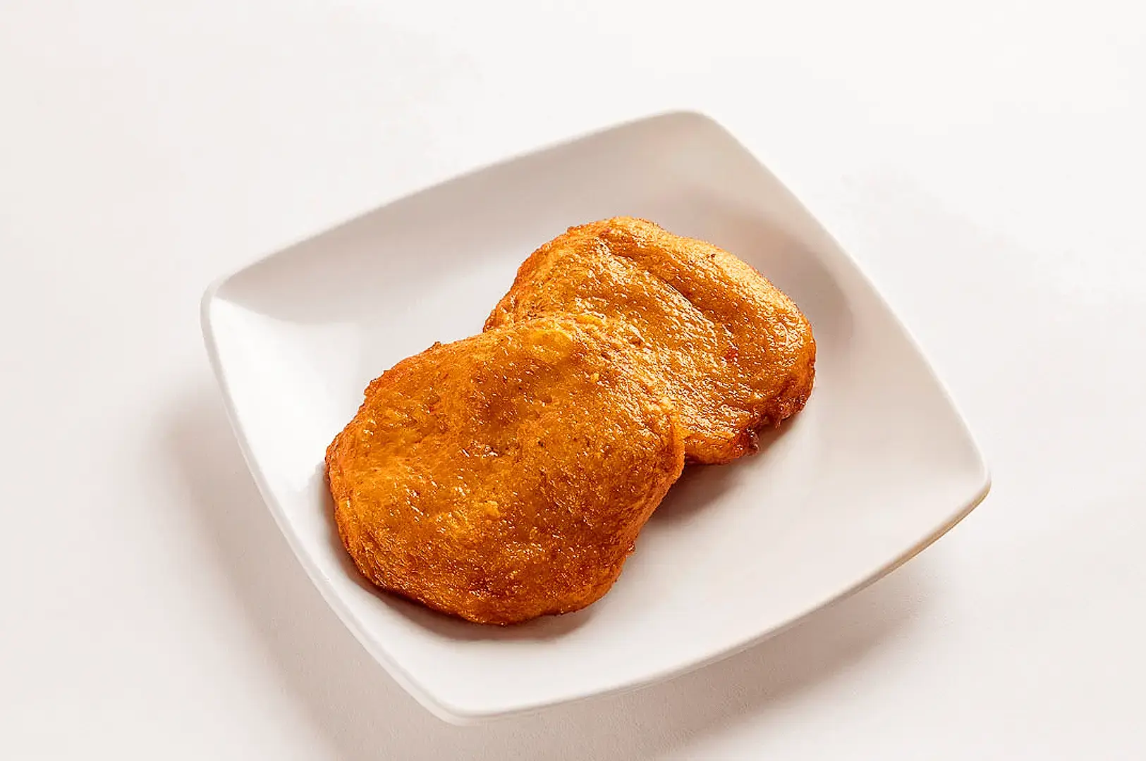 Thai restaurant appetizer featuring two golden fried fish cakes served on a white plate