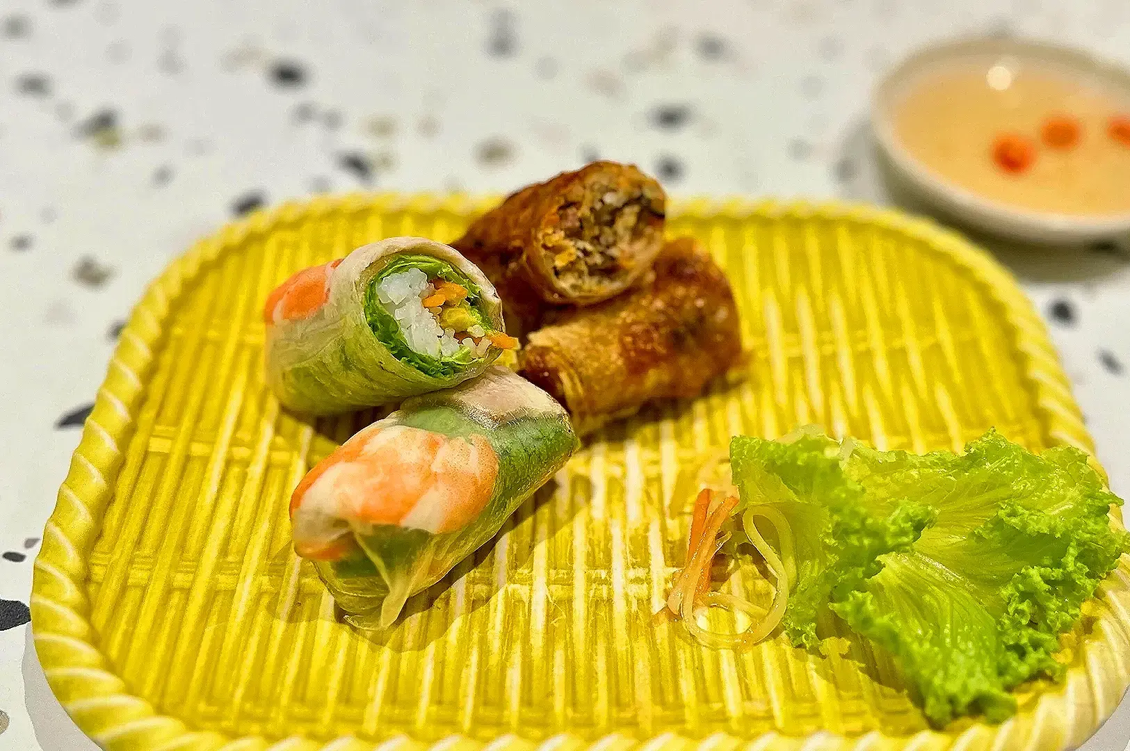 Vietnamese spring rolls and fried rolls served with lettuce and dipping sauce on a bamboo plate