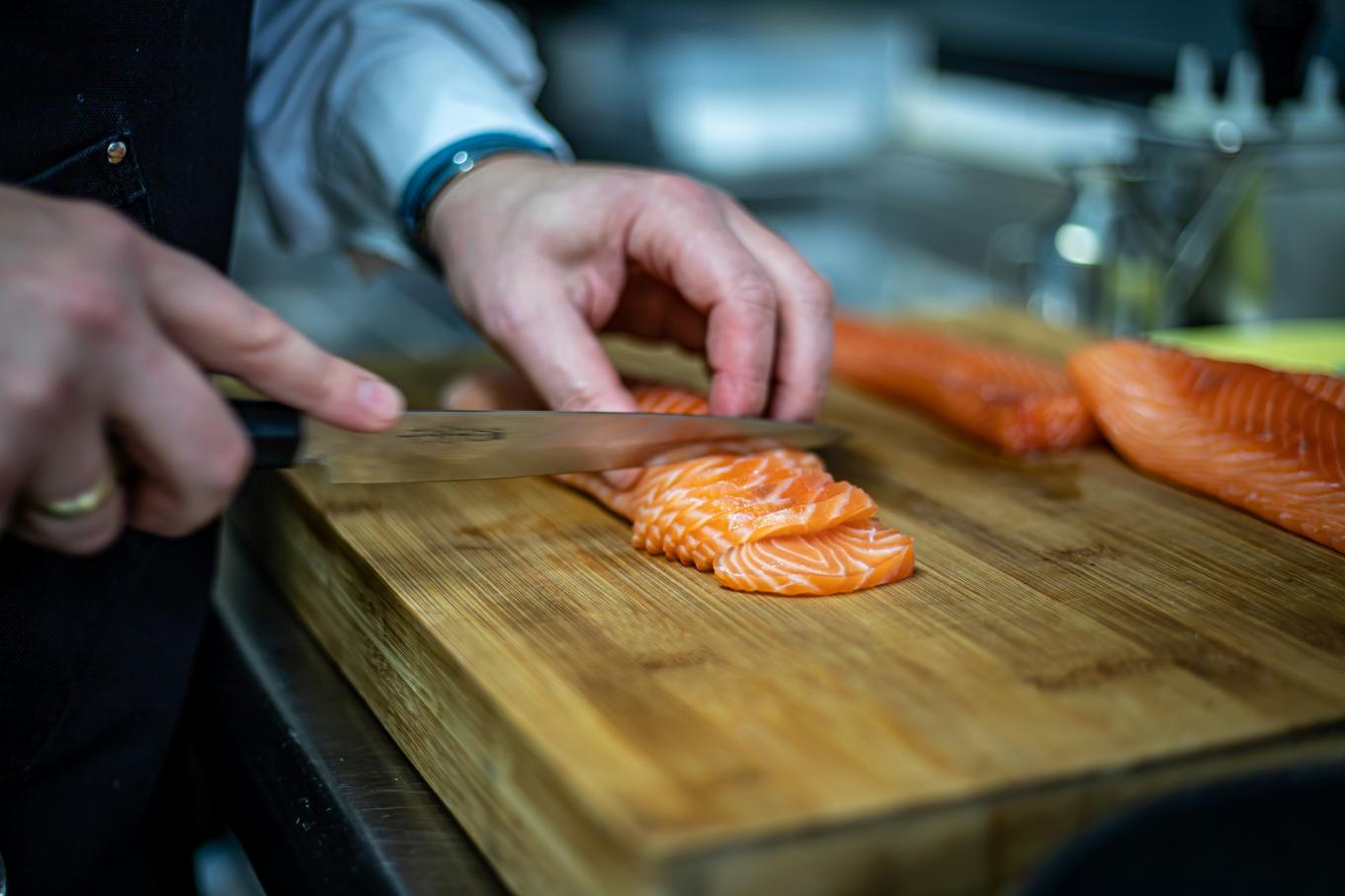 Chef slicing fresh salmon fillet on a wooden cutting board in a kitchen.