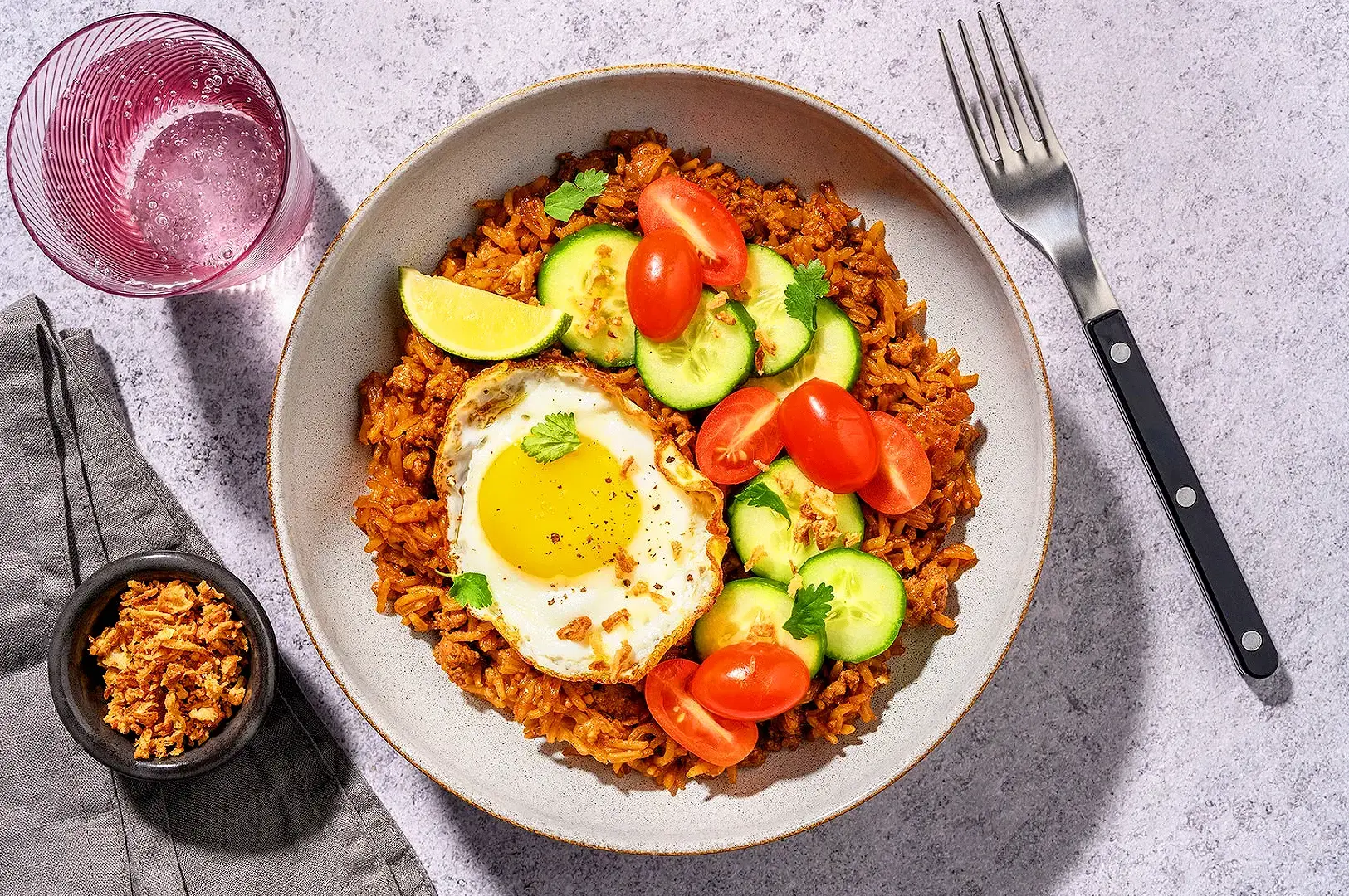 Sambal fried rice served with fried egg, cucumber, chilli and fresh herbs on a plate
