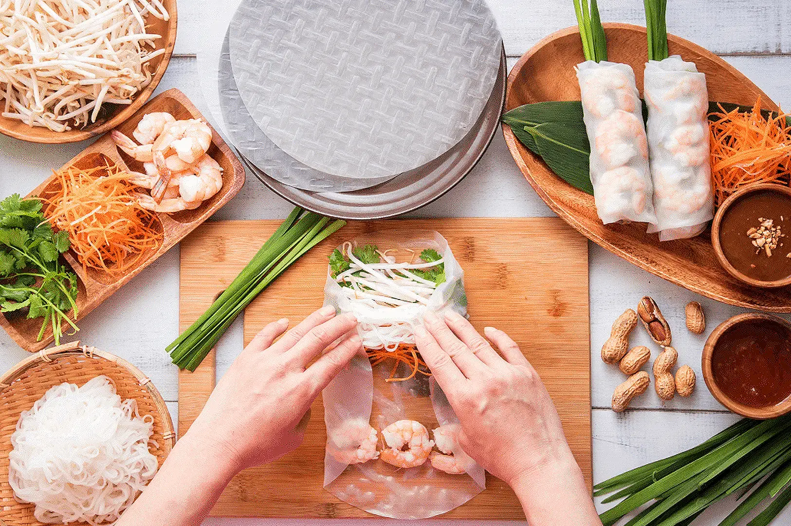 Vietnamese fresh spring rolls being assembled with rice paper, shrimp, rice noodles, herbs and vegetables