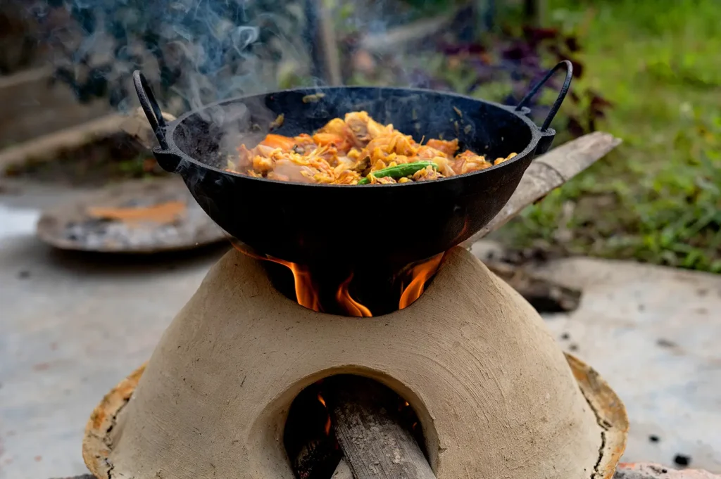 Lao cooking over a traditional clay stove with a smoking wok and wood fire