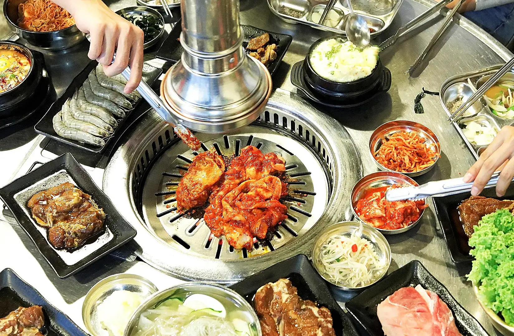 Korean BBQ restaurant table with grilled marinated meat, kimchi, banchan and prawns in Singapore