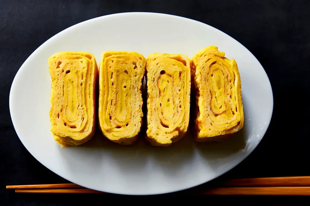 Sliced Japanese tamagoyaki omelette arranged on a white plate with chopsticks