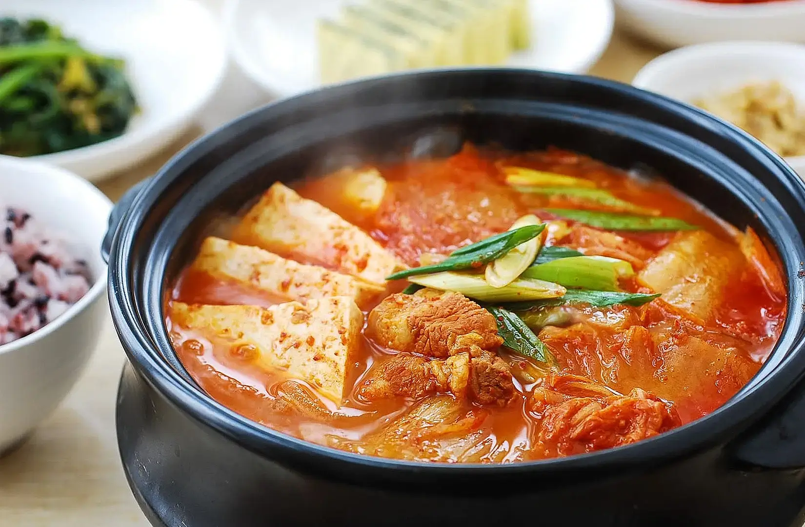 Korean kimchi stew with tofu, pork-style meat and spring onions served in a hot stone pot