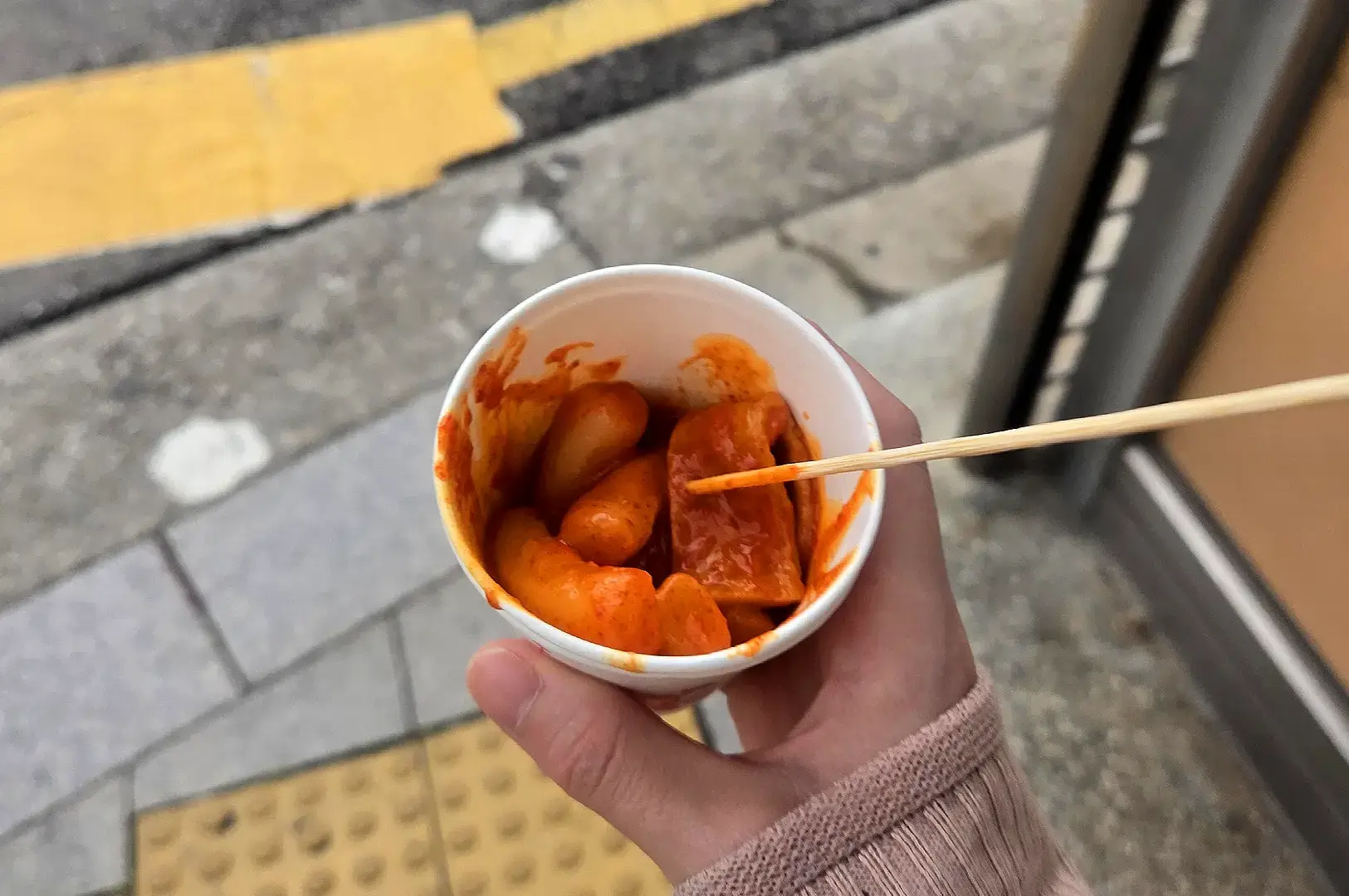 Korean street food tteokbokki and fish cakes served in a takeaway cup with chopsticks